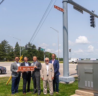 Five men standing at street light with street sign that reads Ruth Colby Boulevard