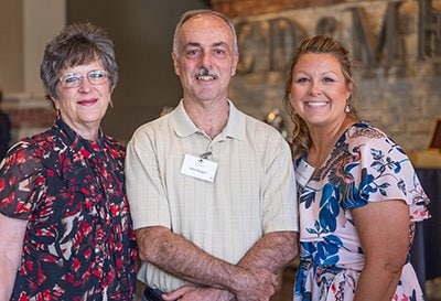 Three people standing smiling at camera. 